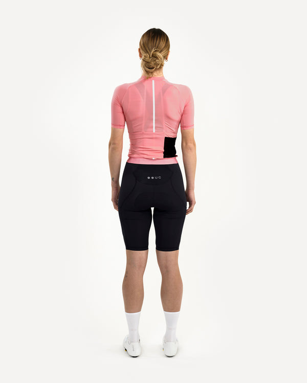 Model wearing the Women's Mono Short Sleeve Jersey in Pink, back view, with black bib shorts and a reflective spine strip.