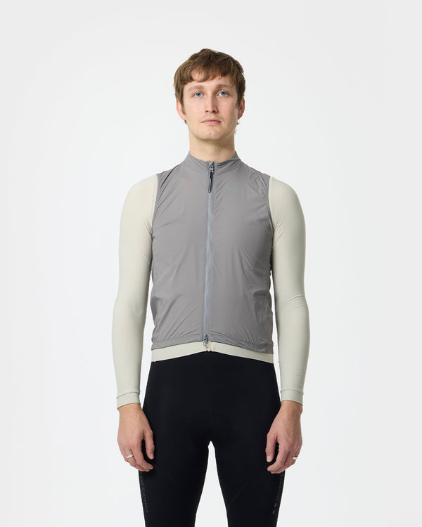 Model wearing the Men's Mono Gilet in Shoot Grey over a cream long-sleeve base layer, paired with black cycling bib shorts.