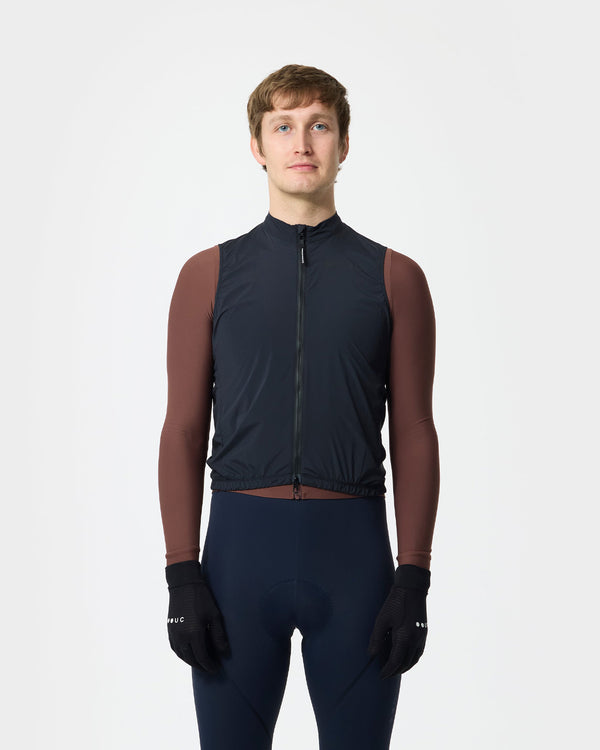 Model wearing the Men's Mono Gilet in Bamboo Black over a Mosswood Brown long-sleeve jersey, navy bib tights and UC gloves.