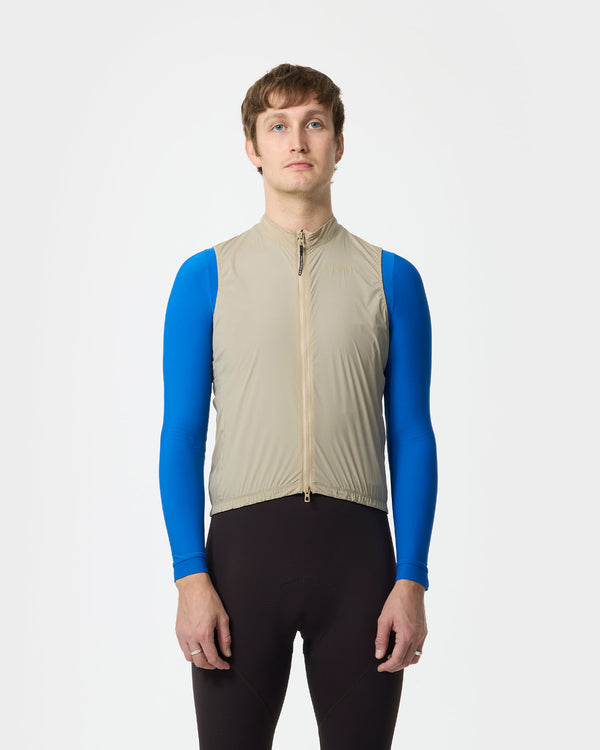 Model wearing the Men's Mono Gilet in Rice Beige over a cobalt blue long-sleeve base layer and black bib tights.