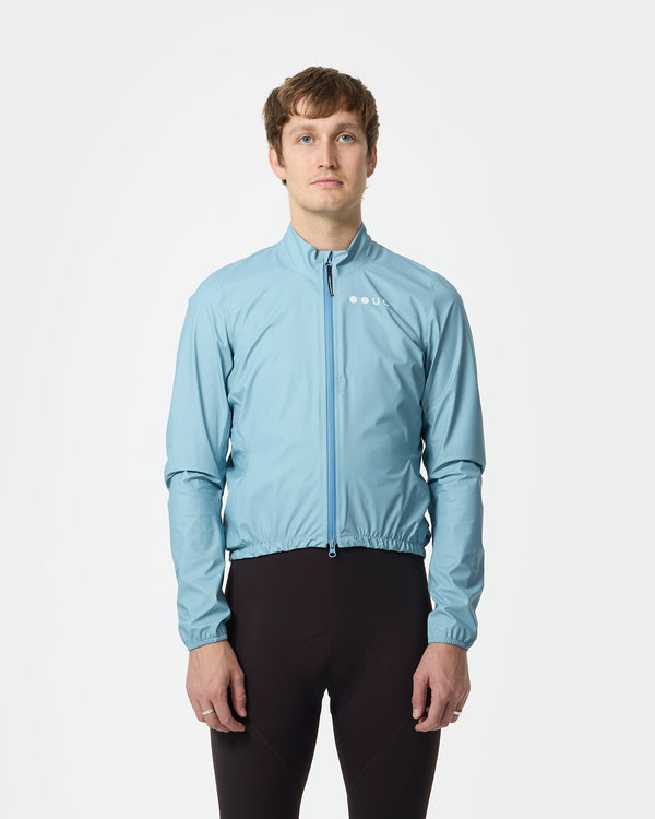 Model wearing the Men's Mono Rain Jacket in Isabel Blue, front view, paired with deep aubergine cycling bib tights.