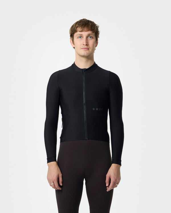 Model wearing the Men's Mono Long Sleeve Jersey in Black, front view, paired with deep oxblood cycling bib tights.
