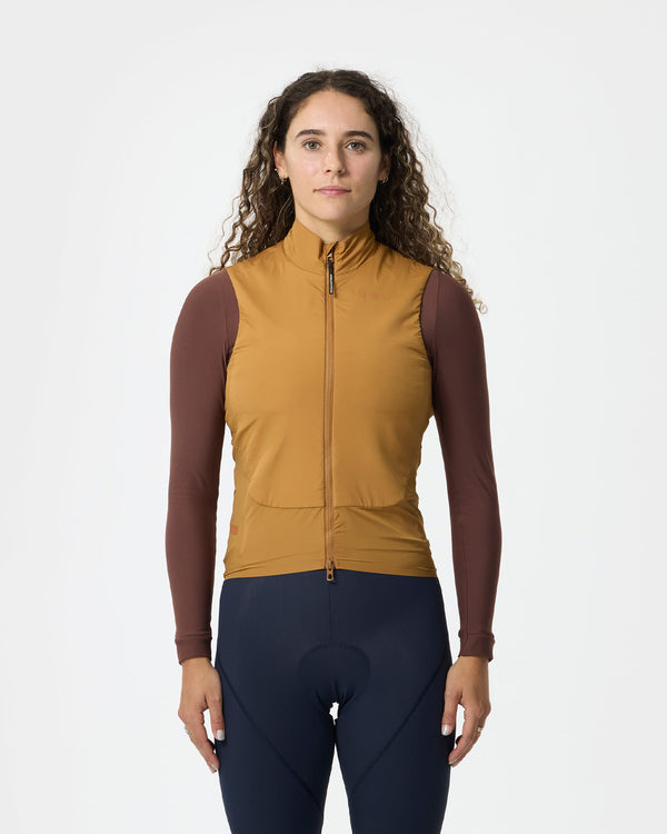 Model wearing the Unisex Chroma Insulated Gilet in Golden Beige over a chocolate-brown jersey and navy bib tights.