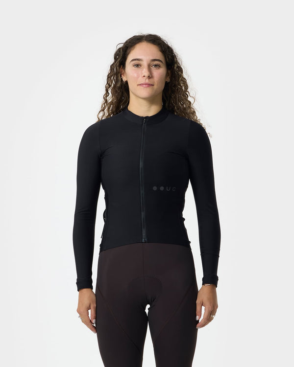 Model wearing the Women's Mono Long Sleeve Jersey in Black, front view, paired with deep burgundy cycling bib tights.