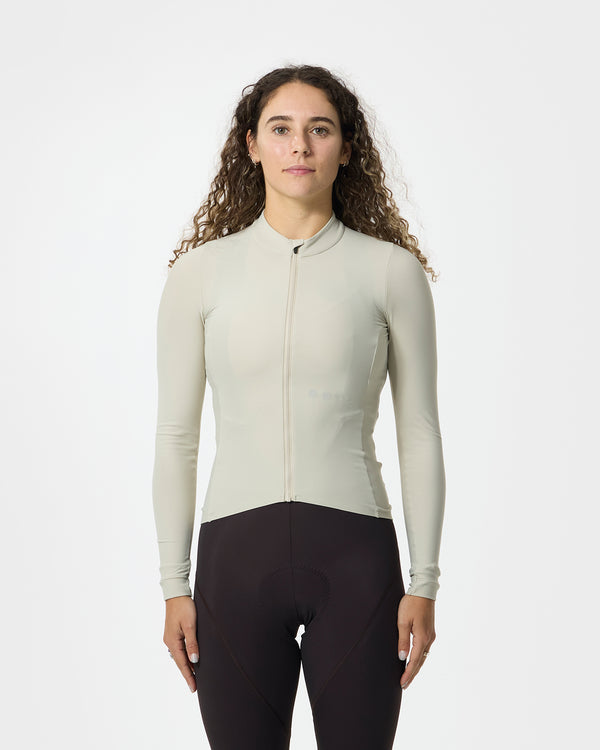 Model wearing the Women's Mono Long Sleeve Jersey in Stone White, front view, paired with dark cycling bib tights.