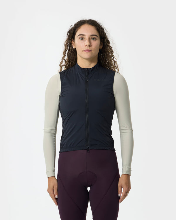 Model wearing the Women's Mono Gilet 2.0 in Bamboo Black over a cream long-sleeve jersey and plum bib tights.