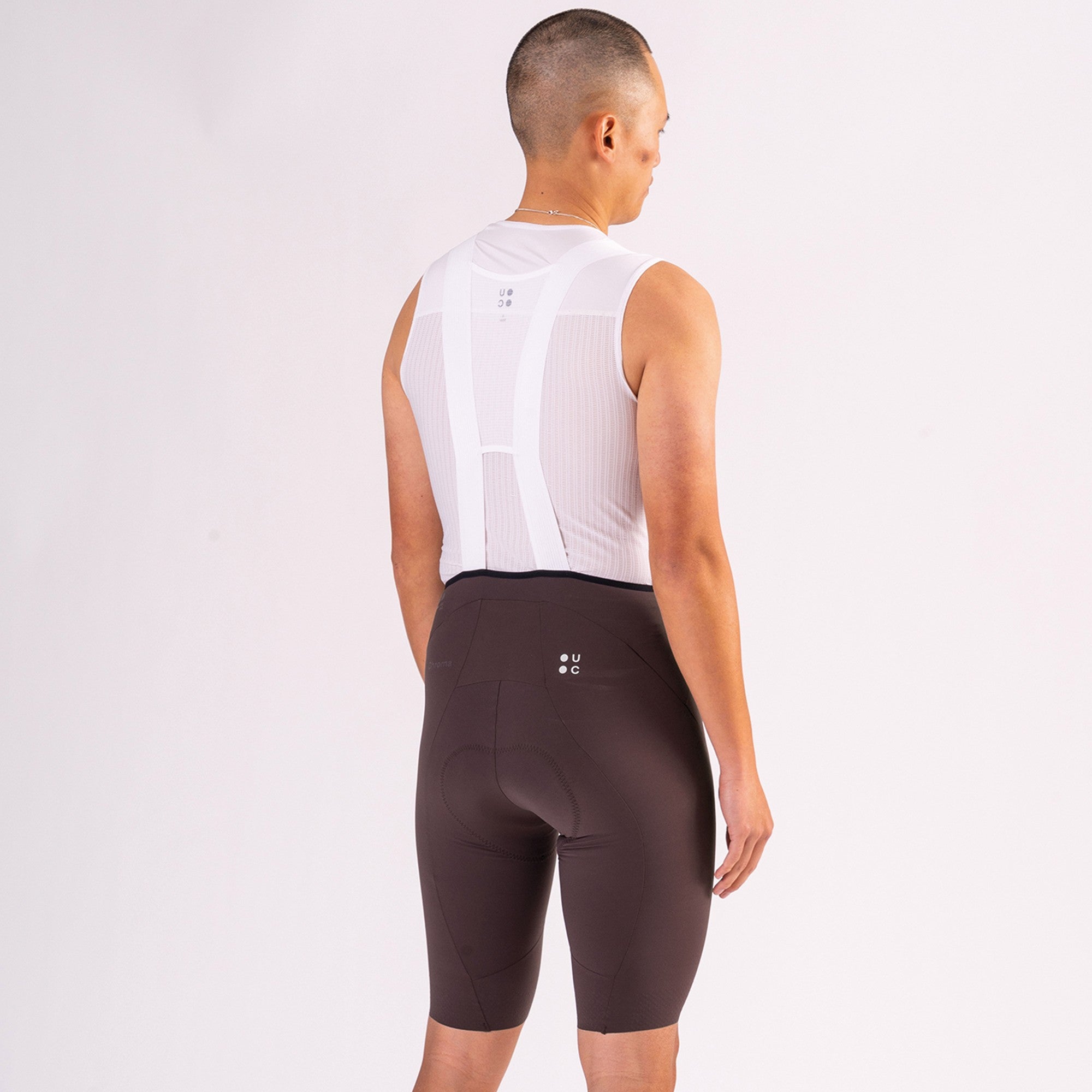 Back view: Men's Chroma Bib Shorts in Heavy Bark Brown with white mesh bib straps and tonal UC rear logo.