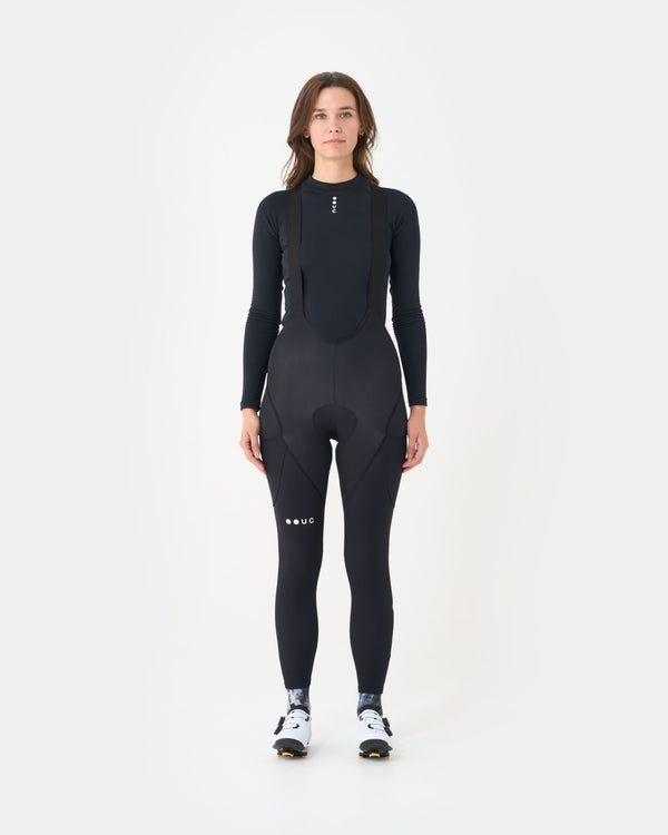 Model wearing the Women's Mono Cargo Bib Tight in Black, front view, with a black UC long-sleeve base layer.