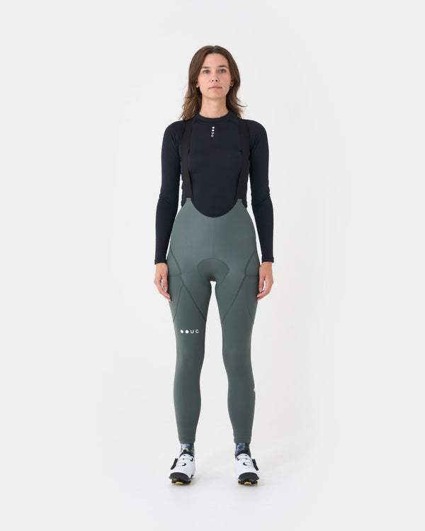 Model wearing the Women's Mono Cargo Bib Tight in Industrial Teal with a black UC base layer and white cycling shoes.