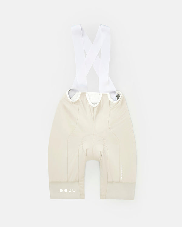 Flatlay of the Women's Mono Bib Shorts 2.0 in Off White: crossover white bib straps, tonal UC hem logo and chamois.